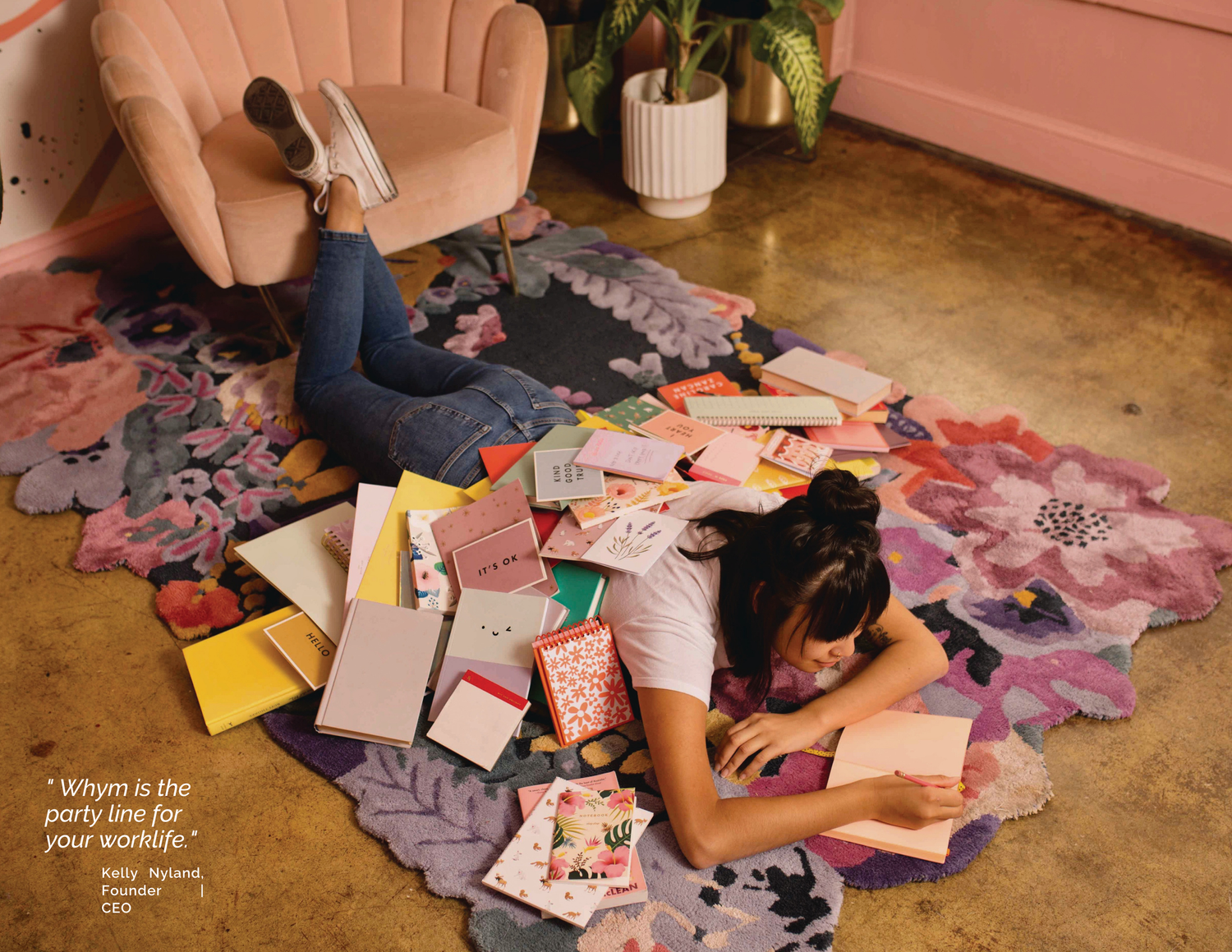Woman lying on a floral rug writing in a pink notebook, surrounded by colorful cards and stationery; quote from Kelly Nyland