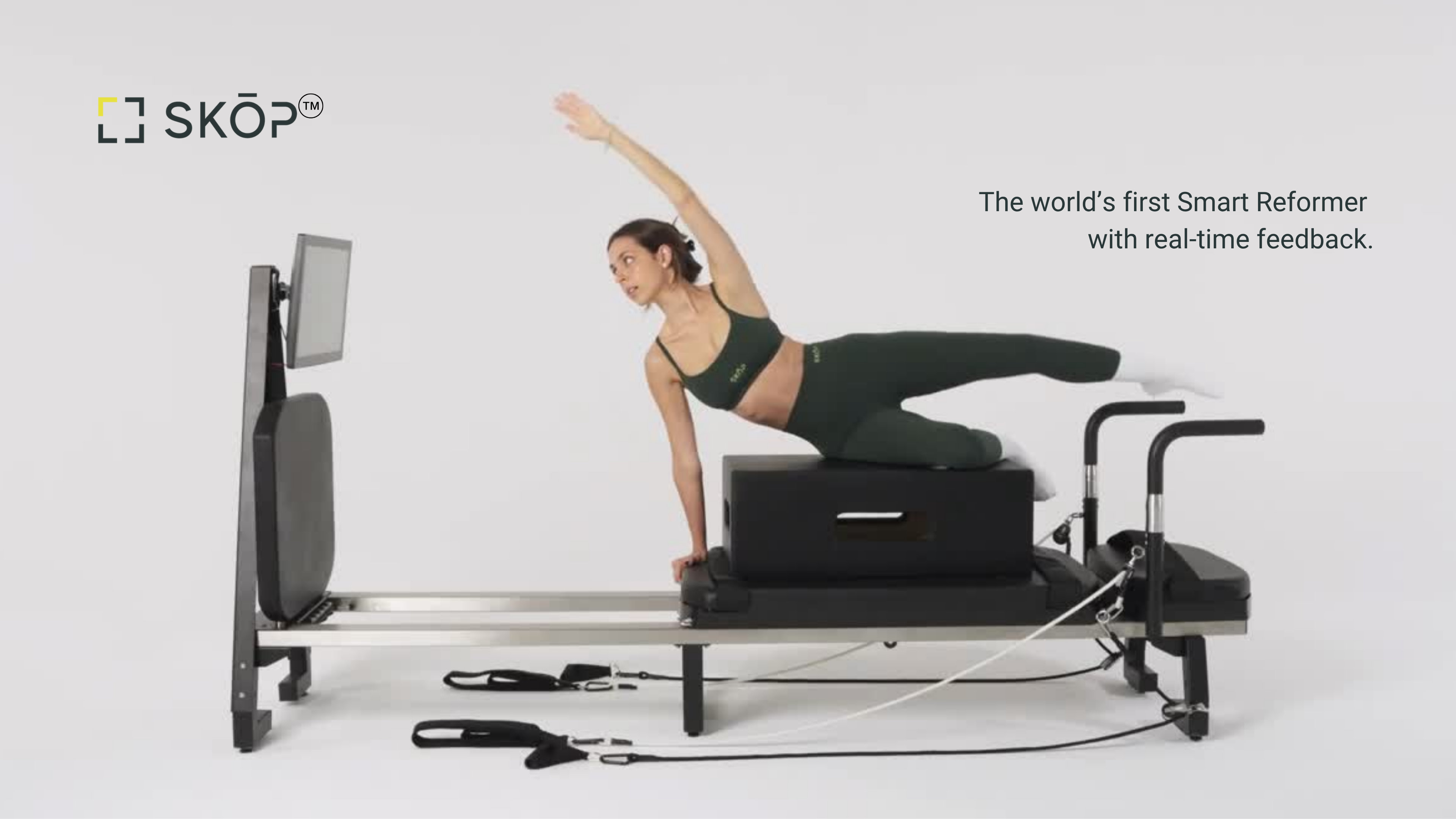 Woman in green activewear doing a side plank on a black Skop reformer facing a screen; text reads "The world's first Smart Reformer with real-time feedback"