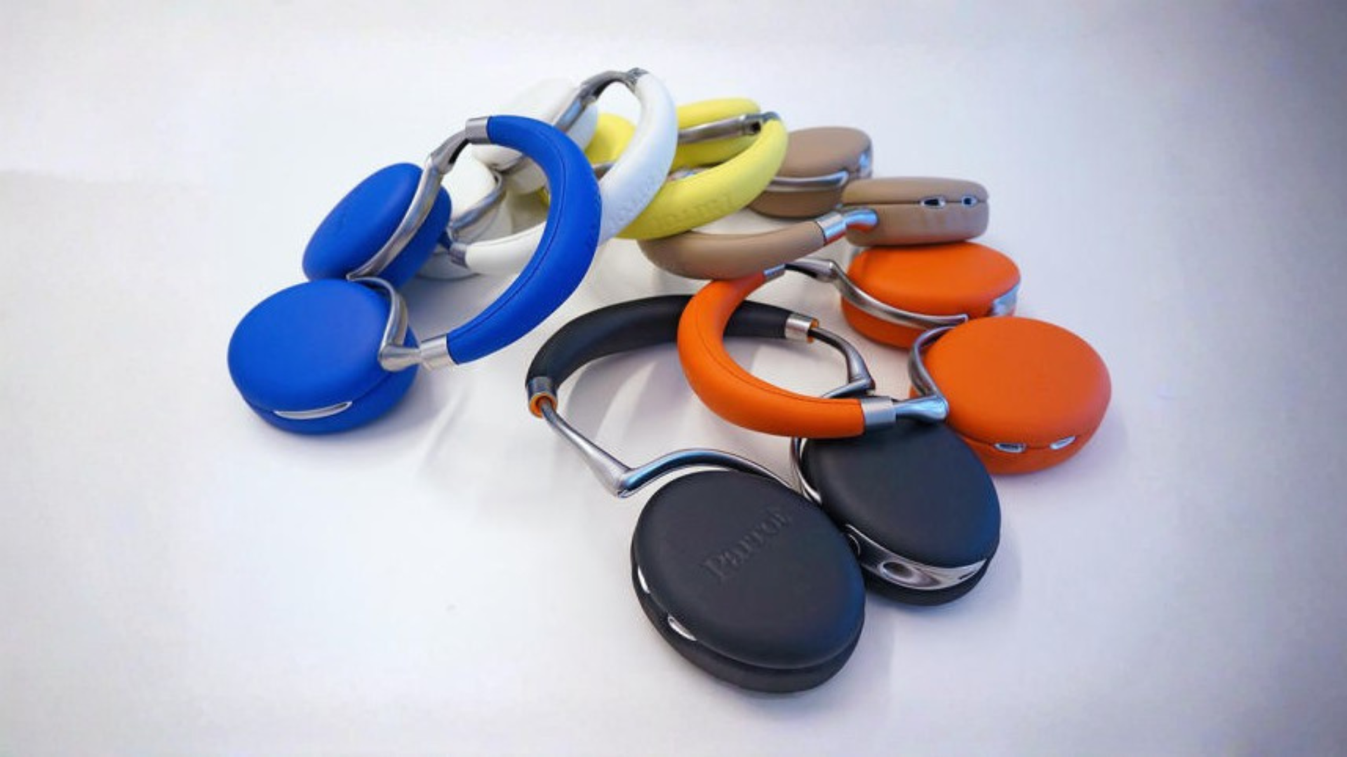 Pile of Parrot Zik headphones in blue, white, yellow, tan, orange and black on a white surface.
