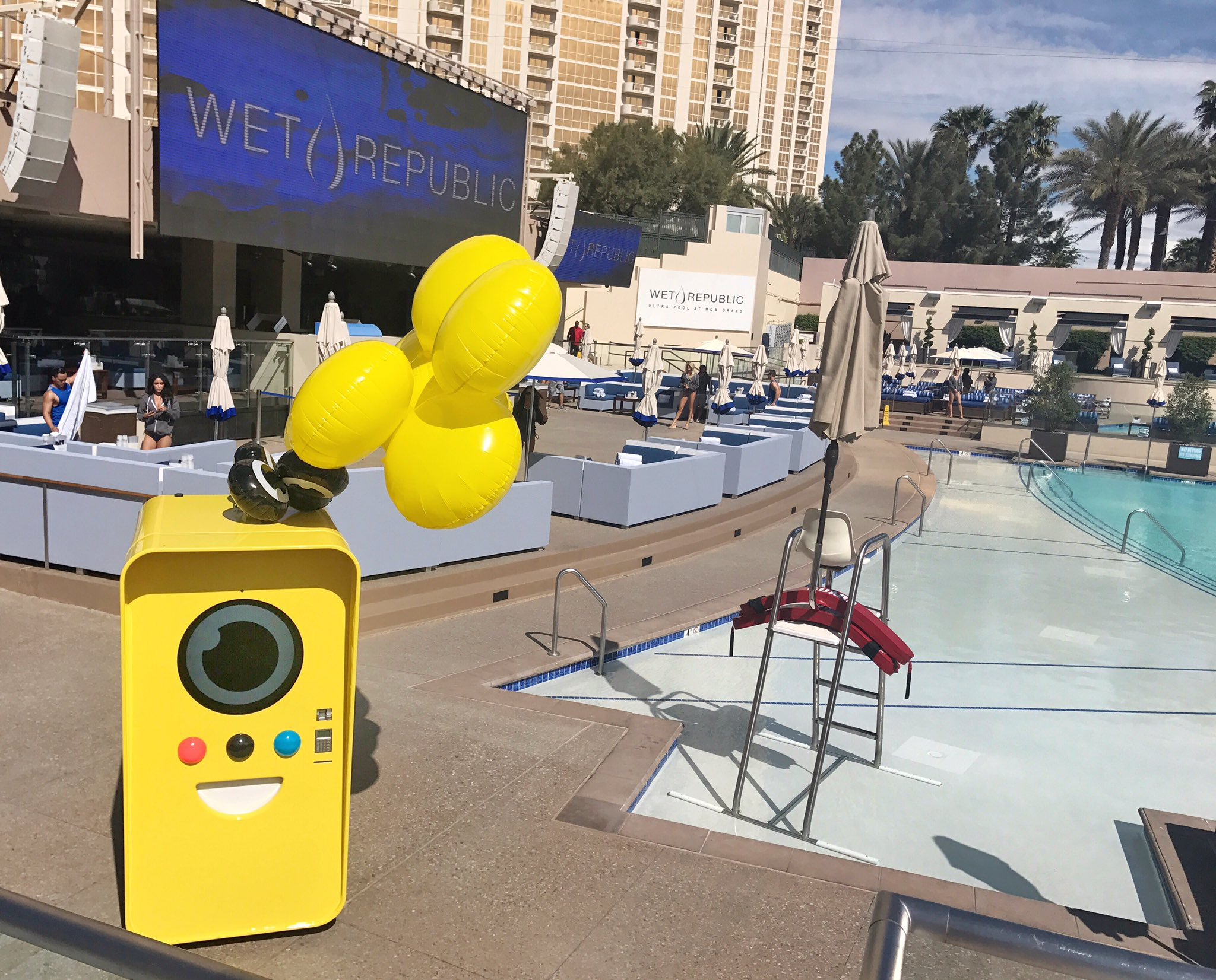 Yellow Snapbot machine with balloons at a pool, Wet Republic screen and lifeguard chair behind