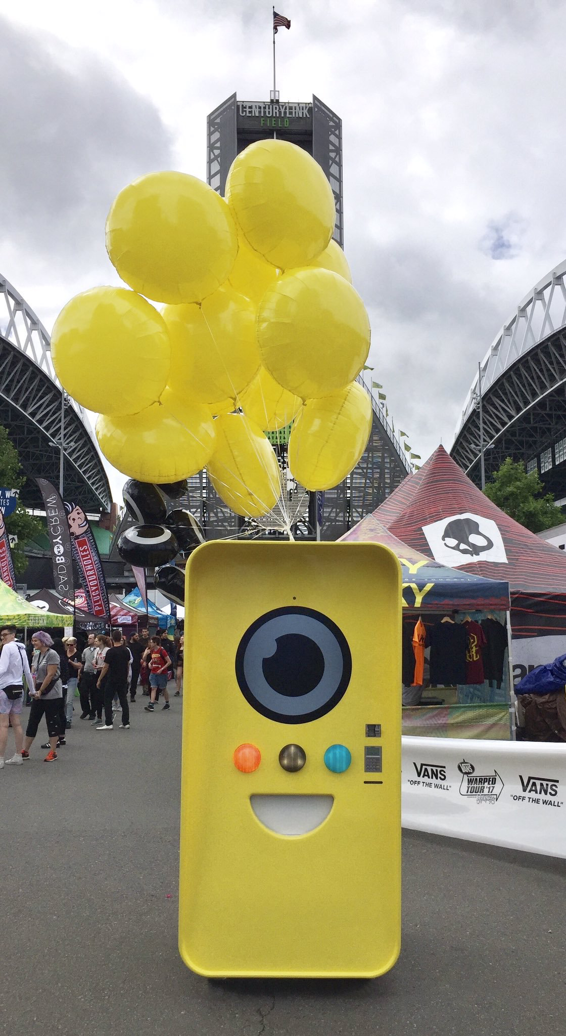 Yellow Snapbot Spectacles machine with balloons at Vans Warped Tour, CenturyLink Field and merch tents behind