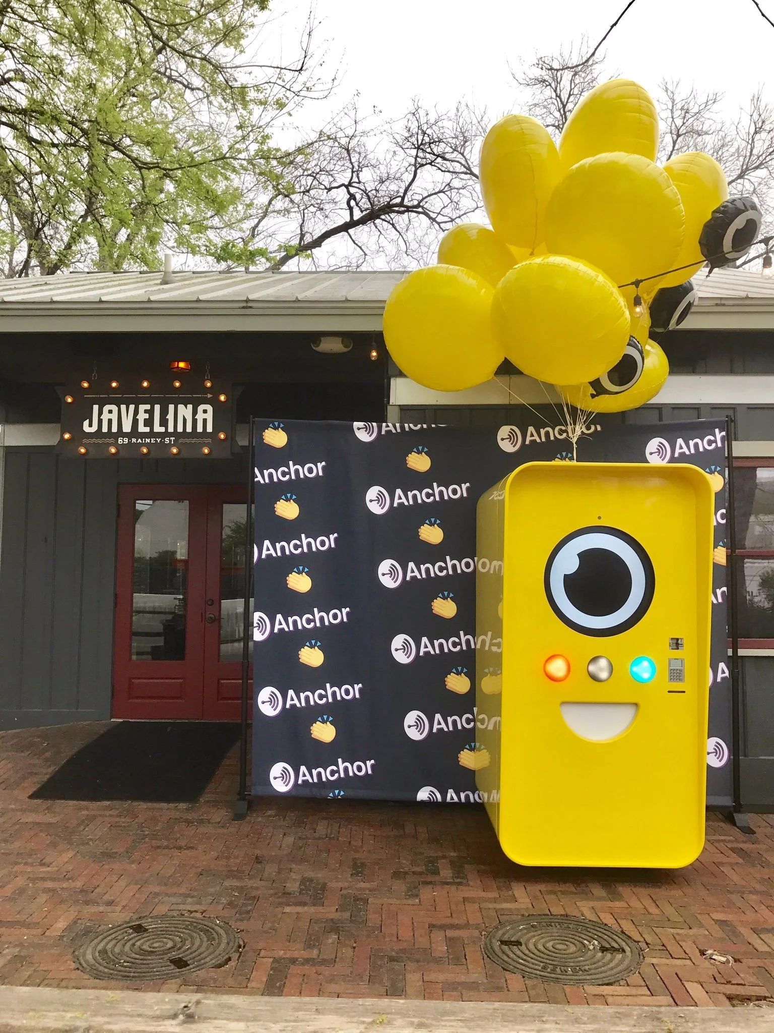 Yellow Snapbot vending machine with a smiling face and yellow balloons by an Anchor step-and-repeat outside Javelina bar