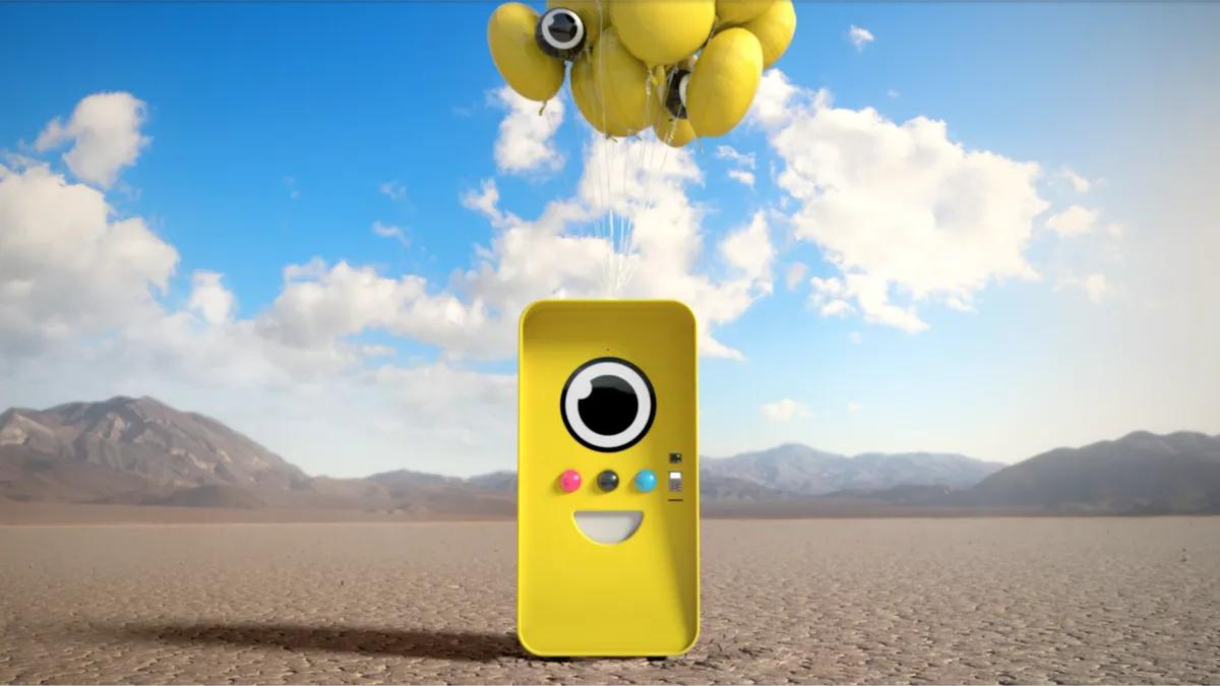 Yellow Snapbot vending robot with a cartoon face floating under yellow balloons in a desert
