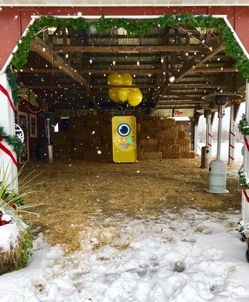 Yellow Snapbot Spectacles vending machine with balloons inside a snowy barn stacked with hay bales, snow falling.