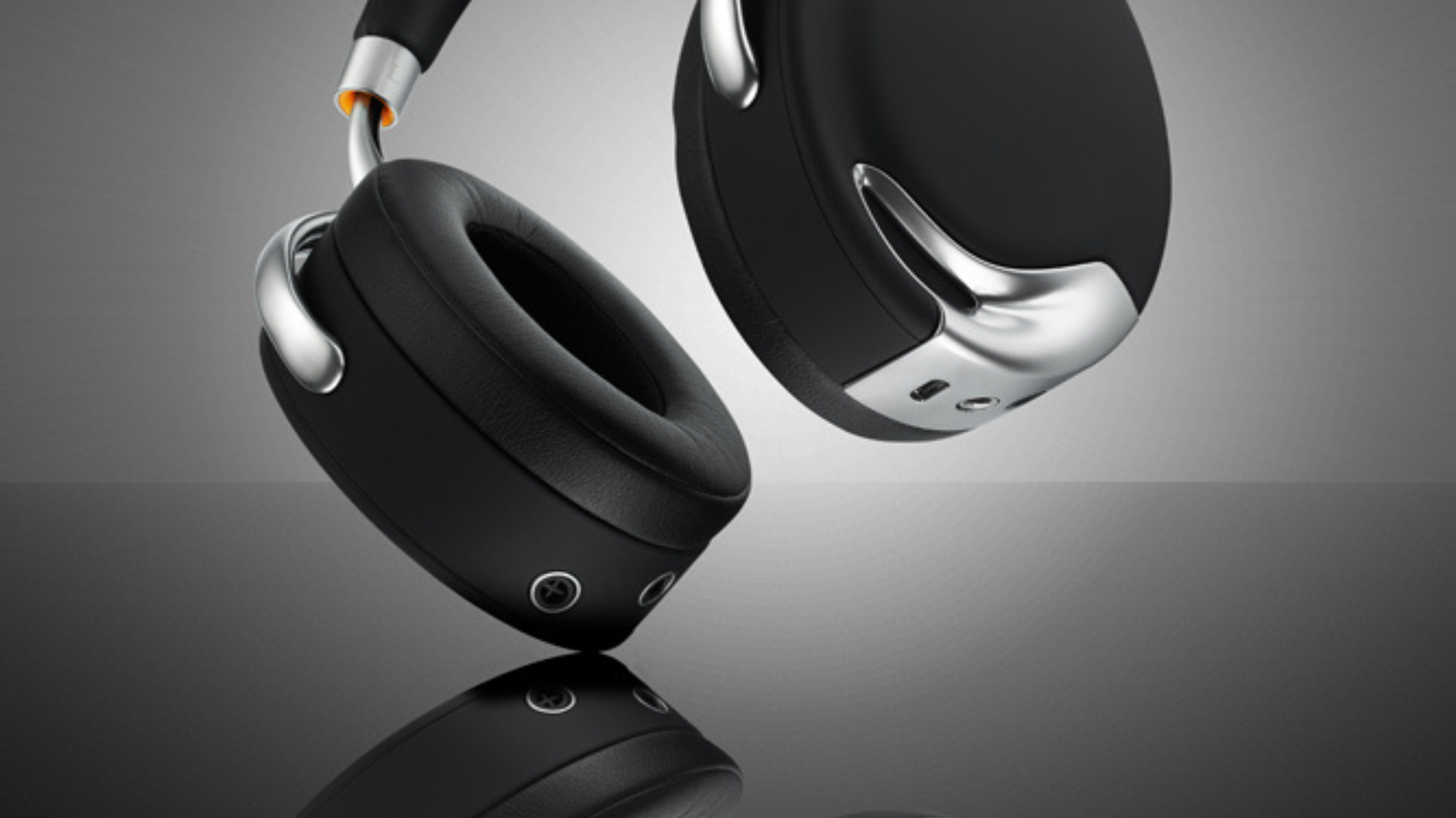 Two black Parrot Zik ear cups with chrome arms on a reflective gray surface, buttons and ports visible.