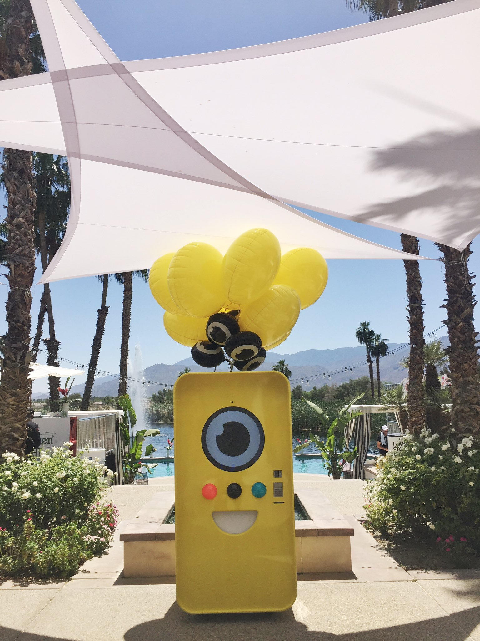 Yellow Snapbot Spectacles vending machine with balloons at a poolside desert party under white shade sails