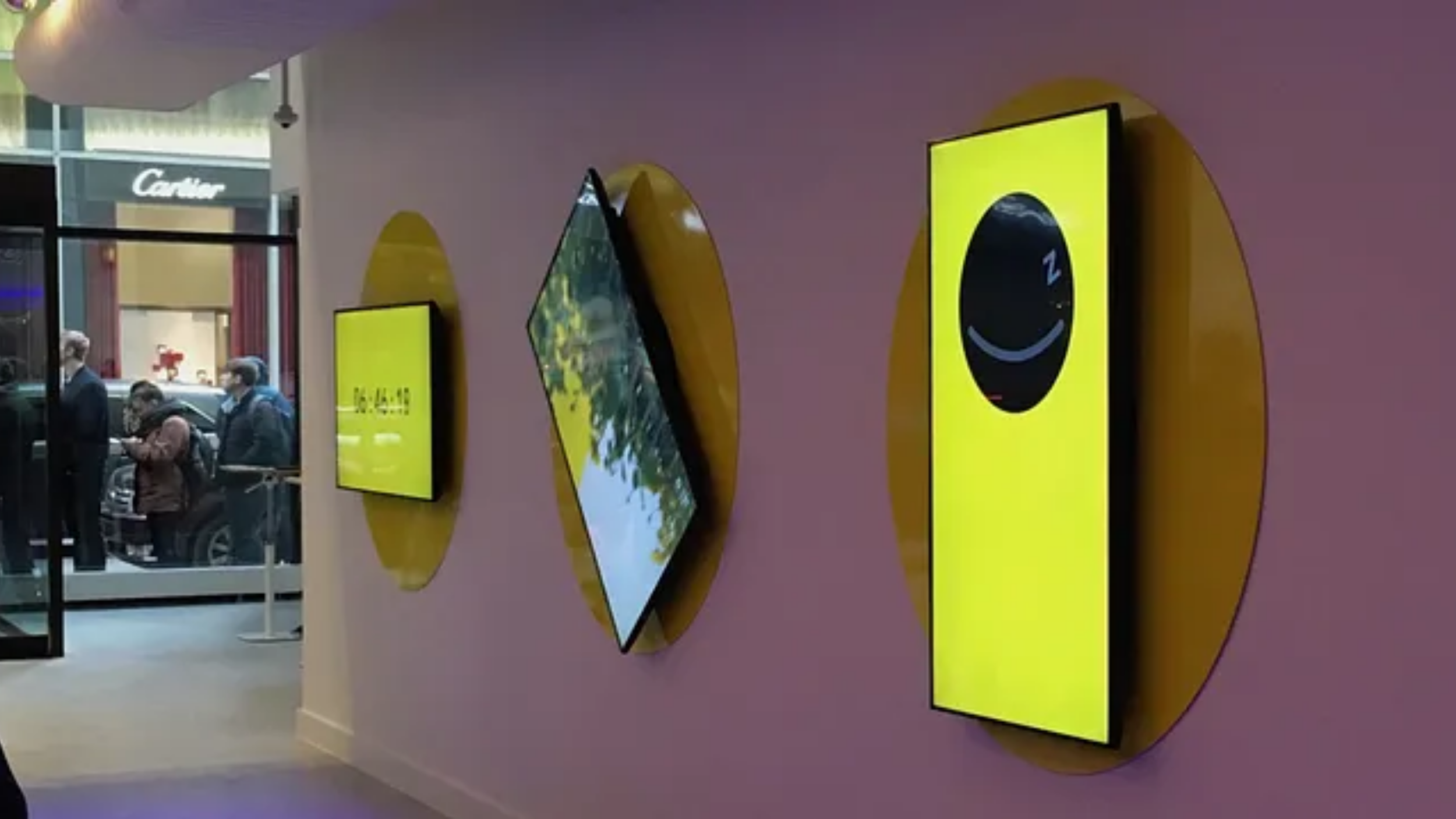 Yellow Snapchat Spectacles display screens mounted on a mall wall near a Cartier storefront