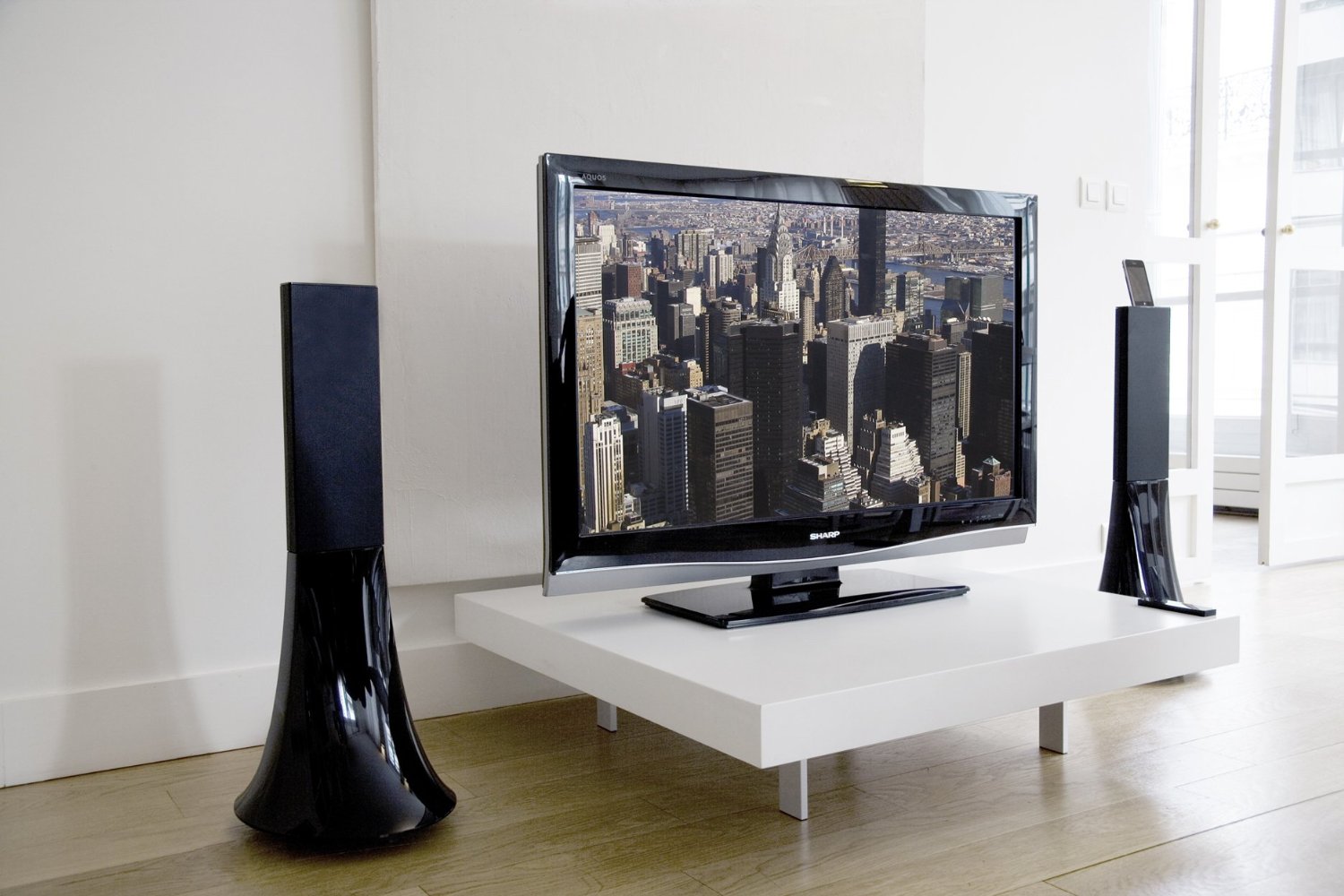 Two tall glossy black Zikmu sculptural speakers flanking a flat-screen TV in a bright modern room