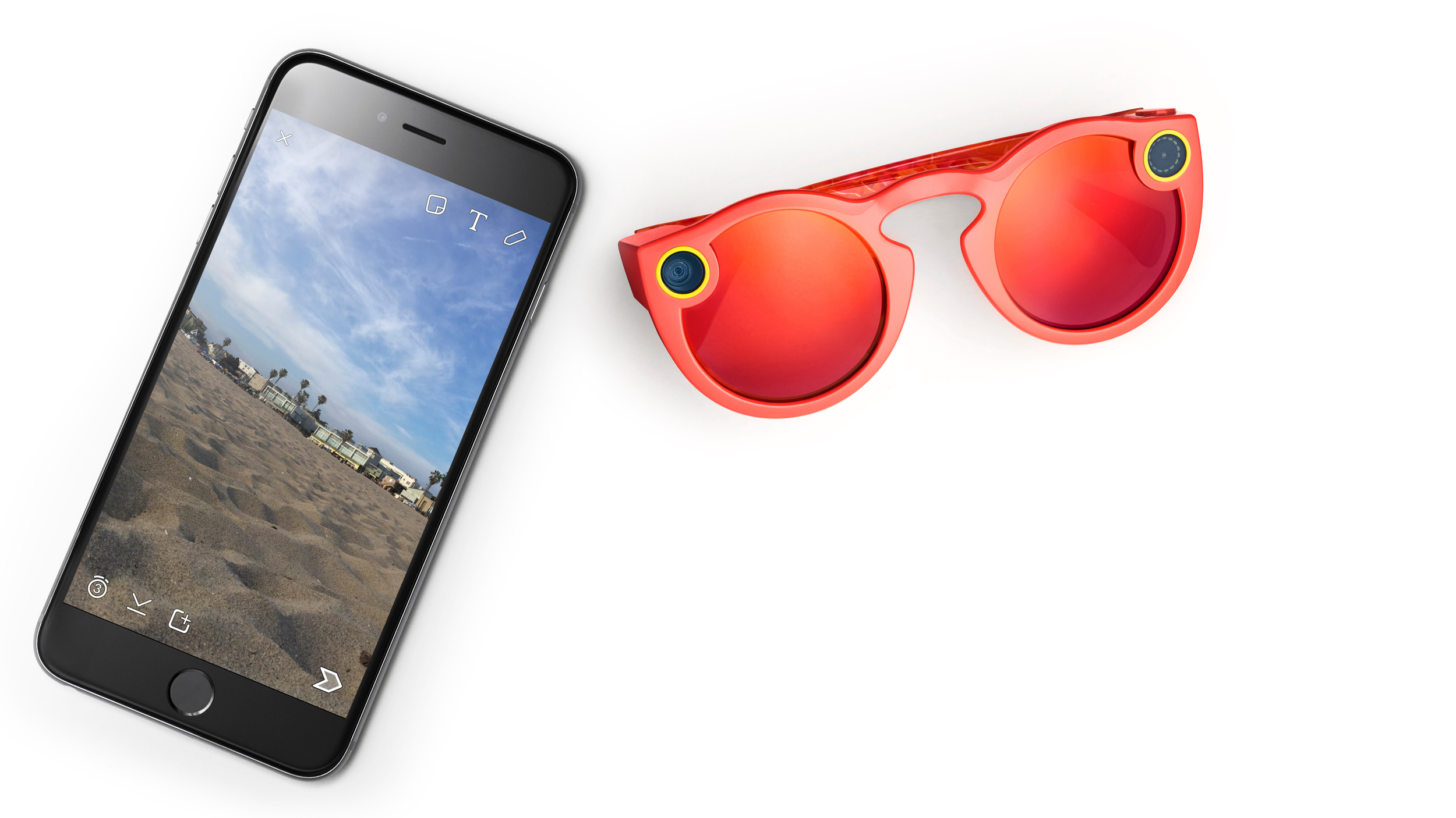 Coral-red Snap Spectacles beside an iPhone showing a beach Snap in the Snapchat camera