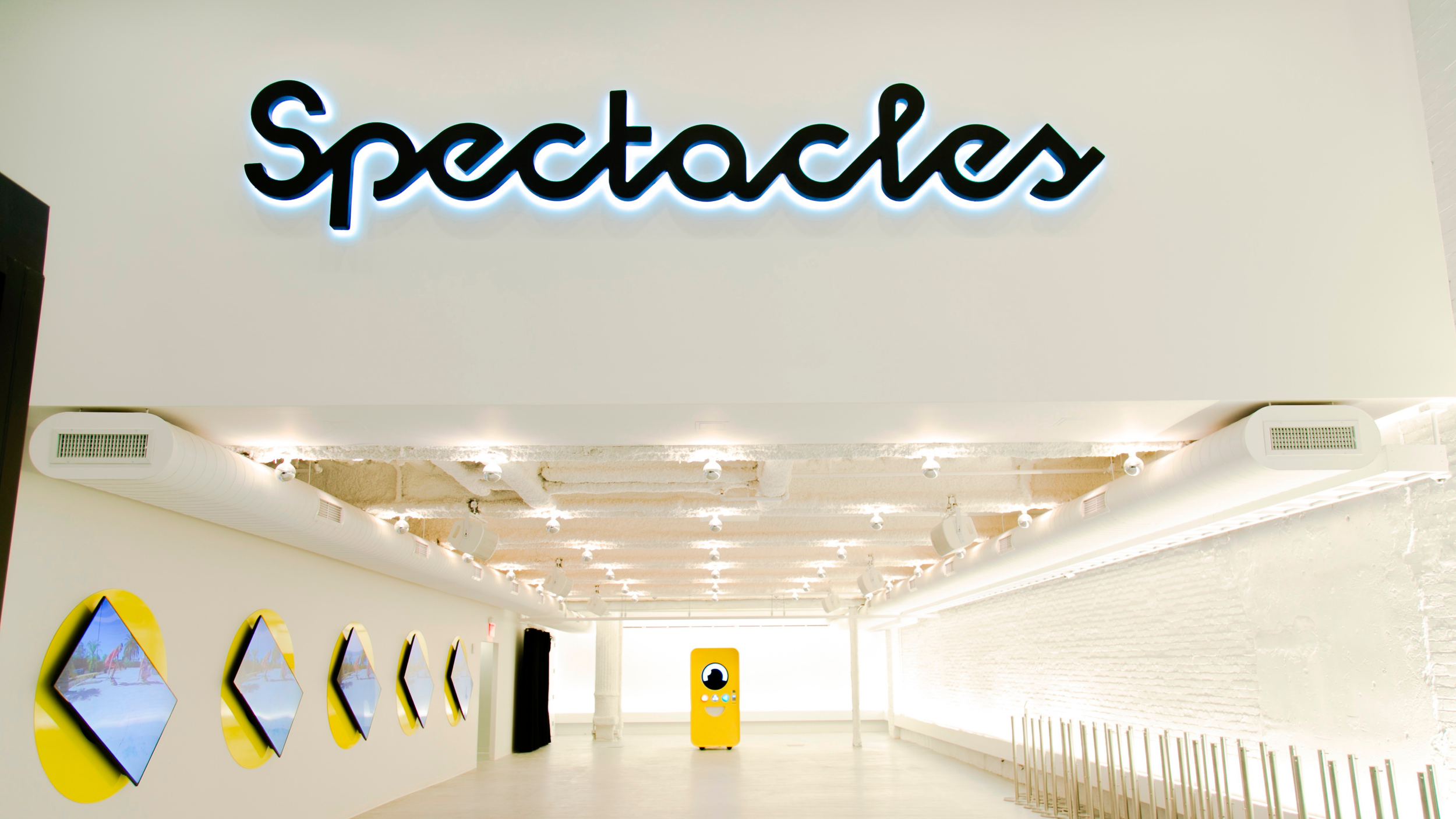 Spectacles pop-up store interior with backlit script logo, diamond wall screens, and a yellow vending machine