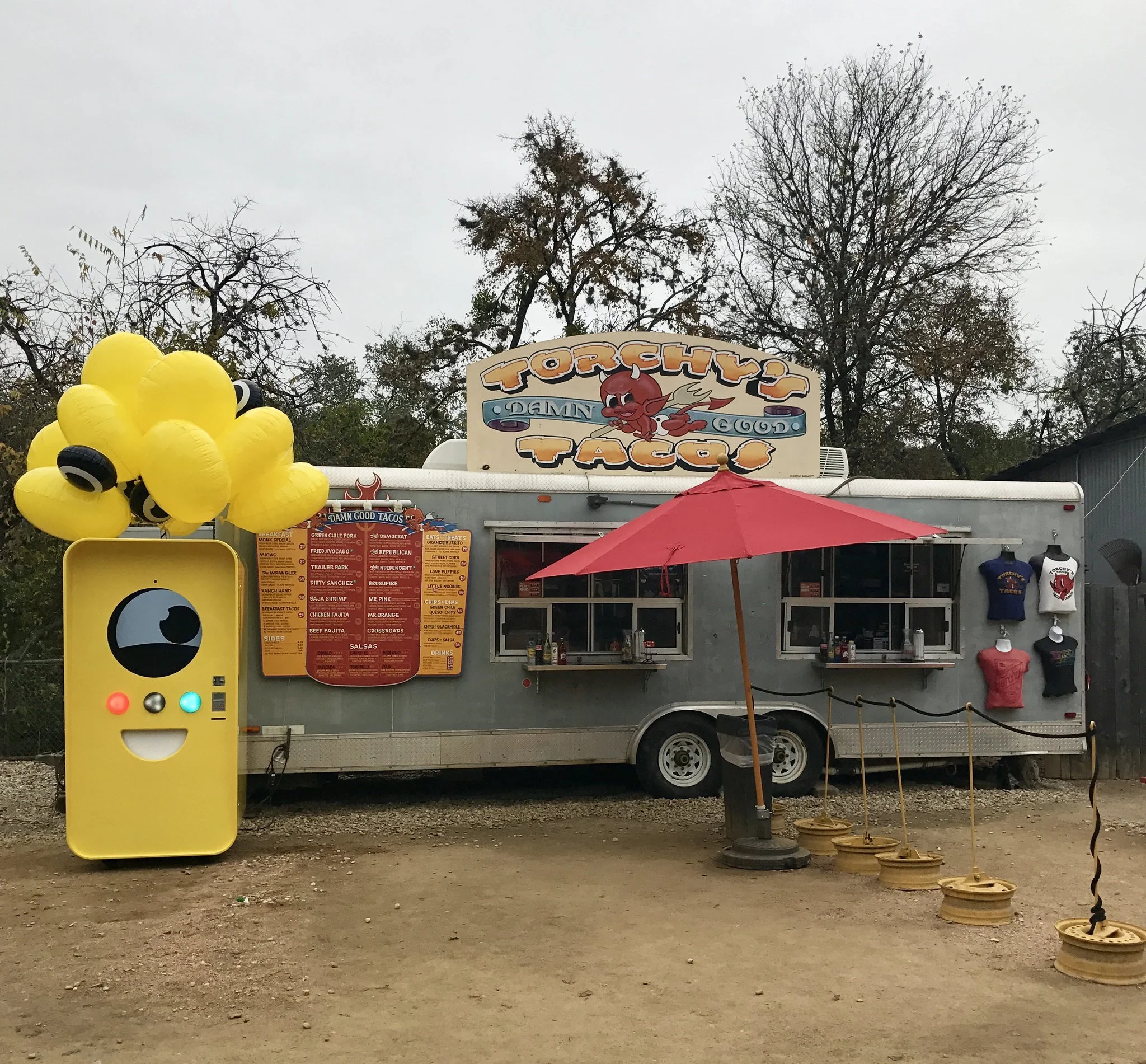 Yellow Snapbot Spectacles vending machine with balloons beside the silver Torchy's Tacos food trailer and its menu.