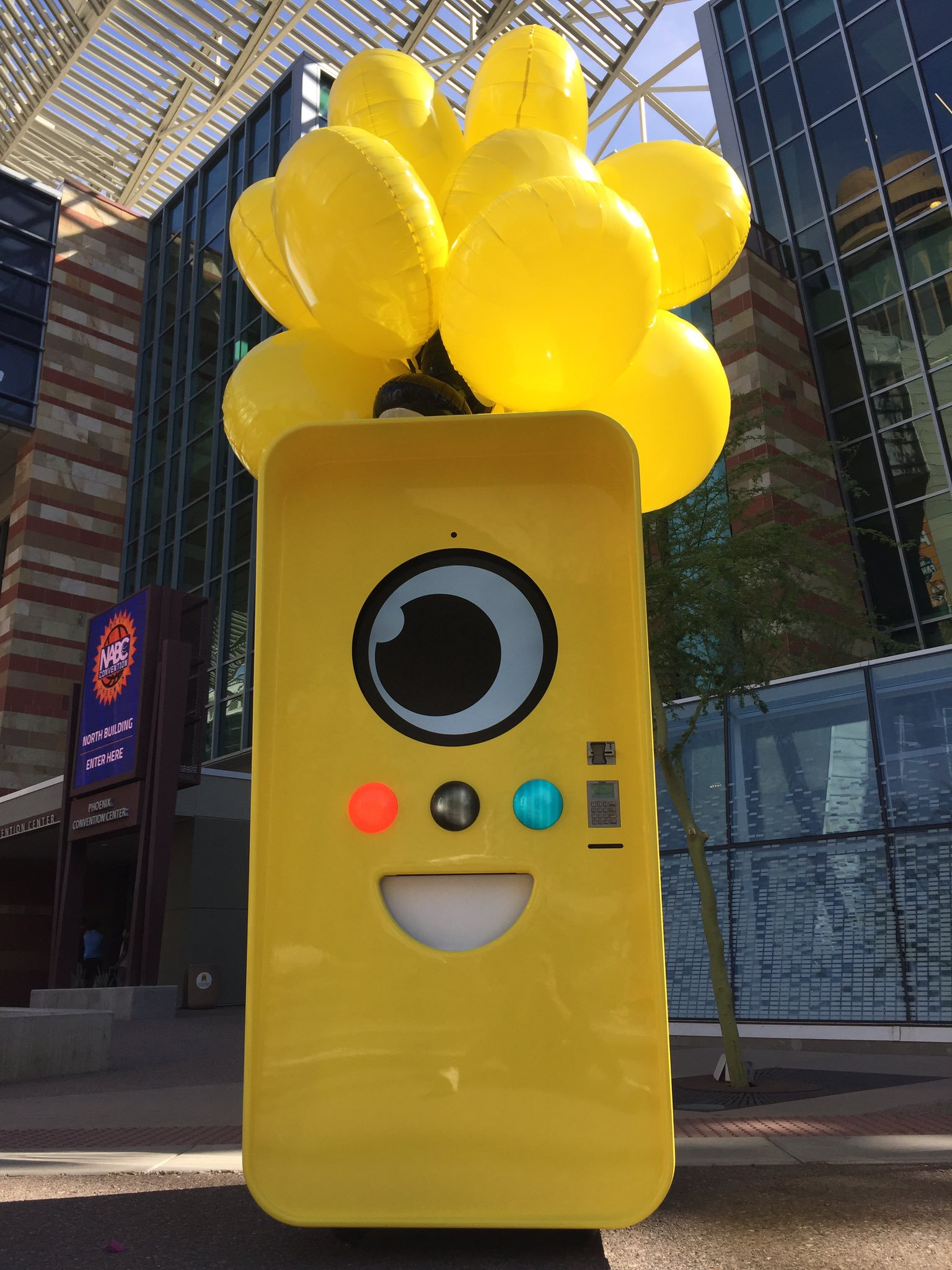 Yellow Snapbot vending machine with balloons outside Phoenix Convention Center near an NABC Convention sign