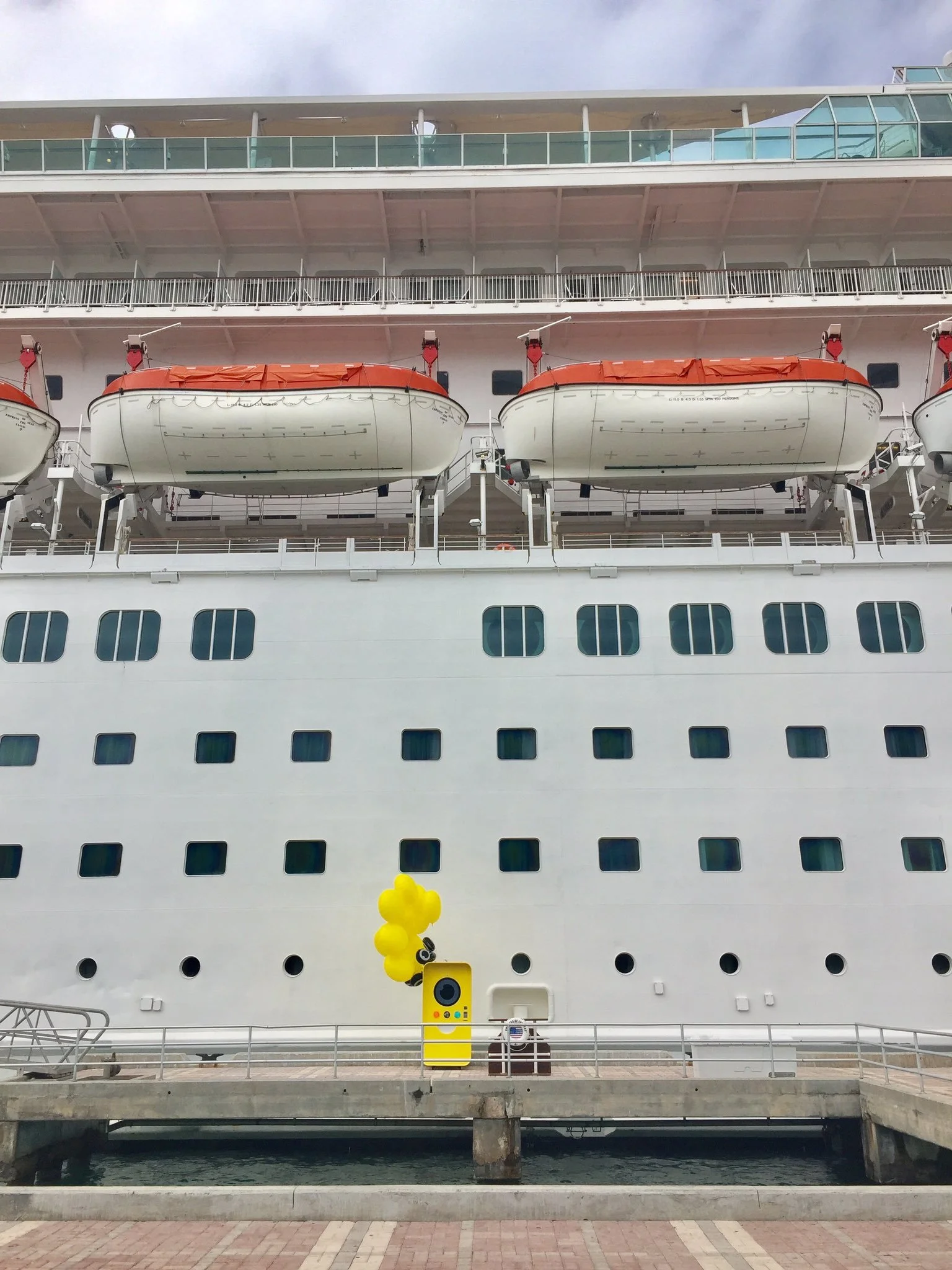 Yellow Snapbot Spectacles vending machine with balloons docked beside a white cruise ship's hull
