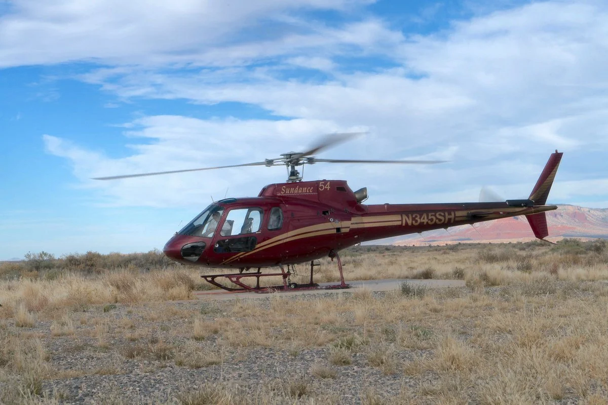 Dark red Sundance helicopter, tail number N345SH, parked on desert scrubland near the Grand Canyon.