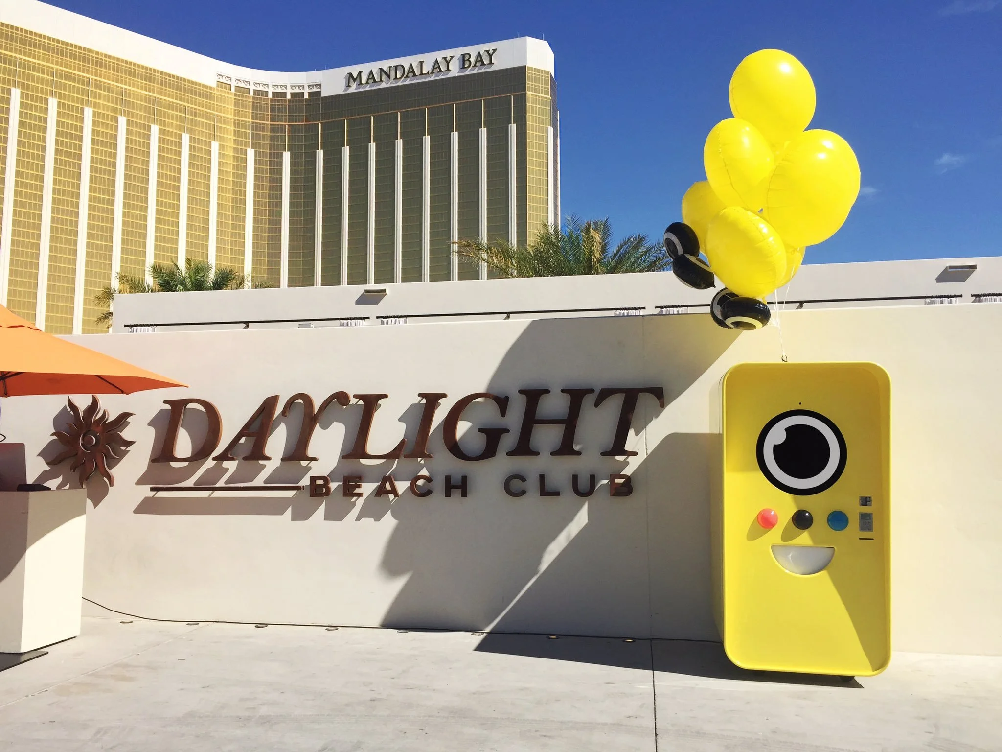 Yellow Snapbot machine with balloons beside Daylight Beach Club sign, Mandalay Bay tower behind
